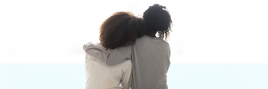 Loving african american single mother sister embrace teen daughter sit on bed looking at window, parent mom hug support protect teenage girl, family trust hope talk understanding concept, rear view